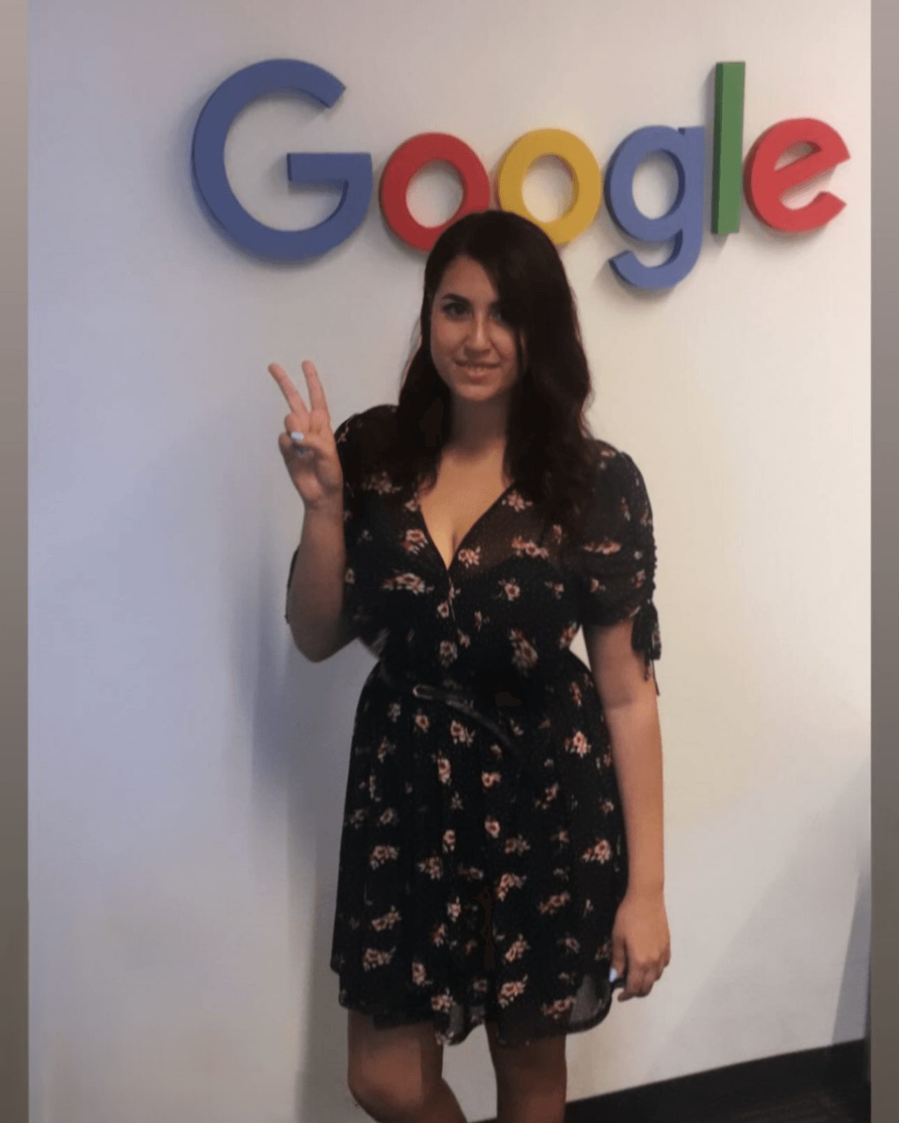 Woman standing in front of a wall with a Google logo, making a peace sign with her right hand.