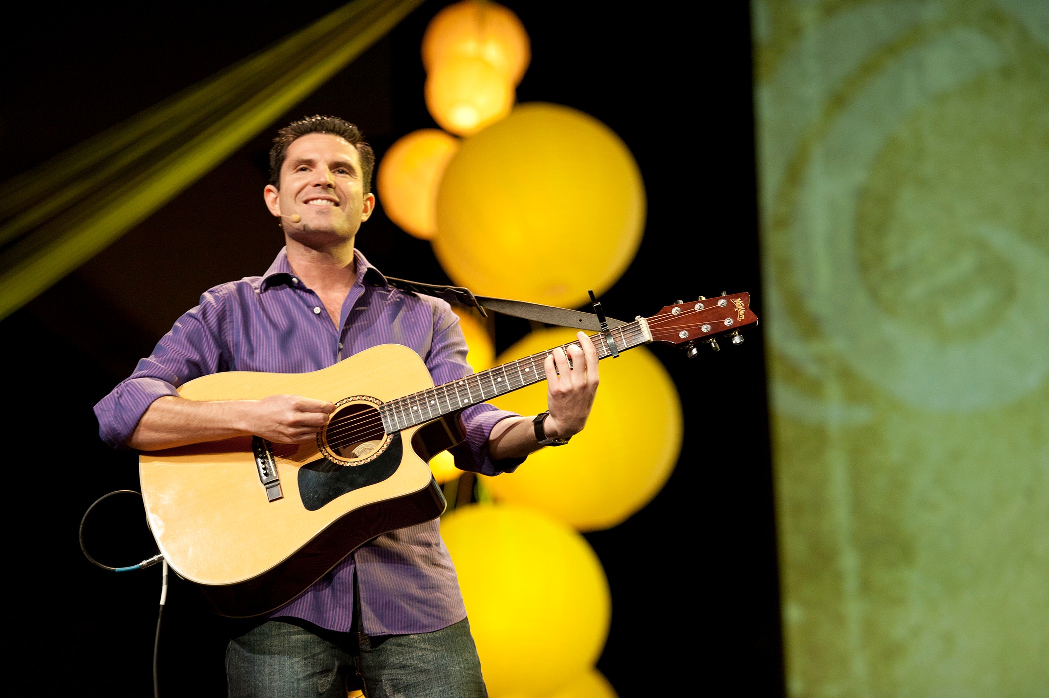 Man playing guitar on stage with yellow spherical decorations in background.
