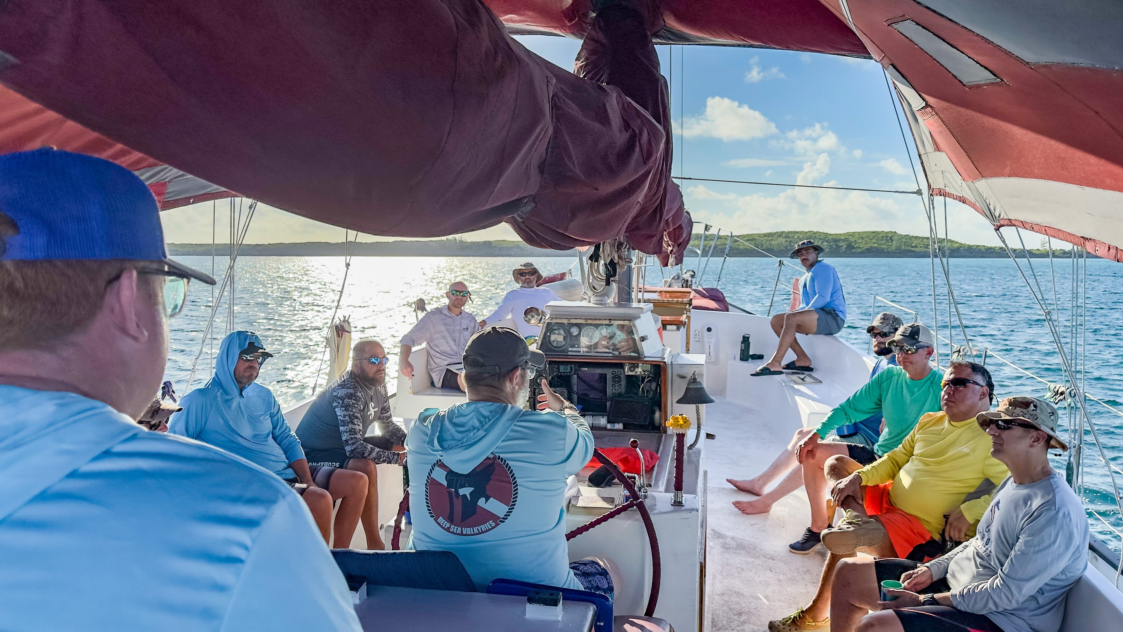 Group of people on a boat enjoying a sunny day on the water, some sitting and some standing, with a view of the lake and sky.