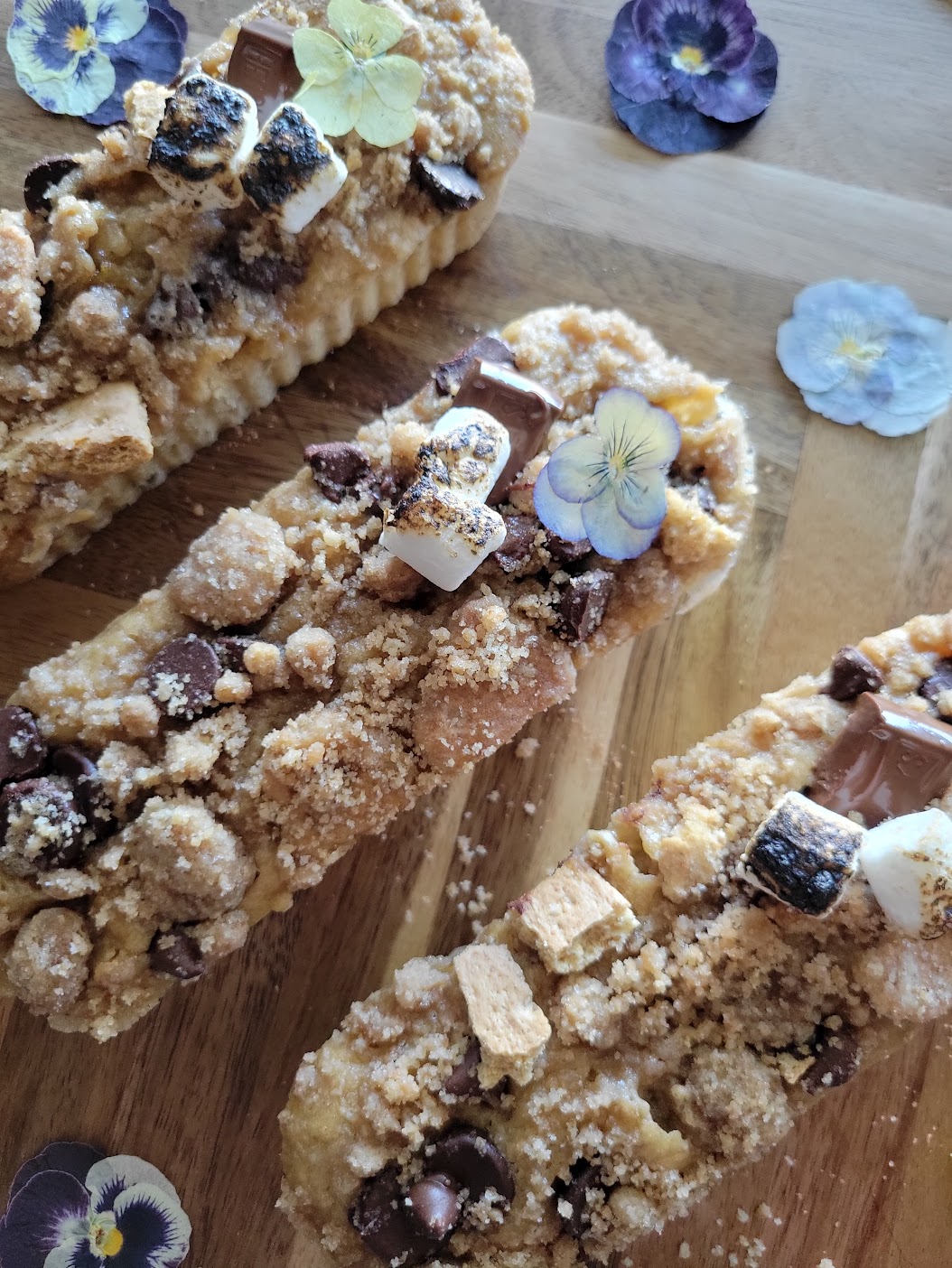 Three rectangular dessert bars with crumbly topping and edible flowers on a wooden surface.