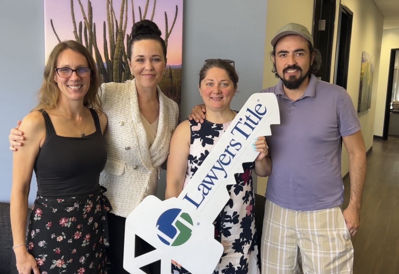 Four people standing together indoors, one holding a sign that says