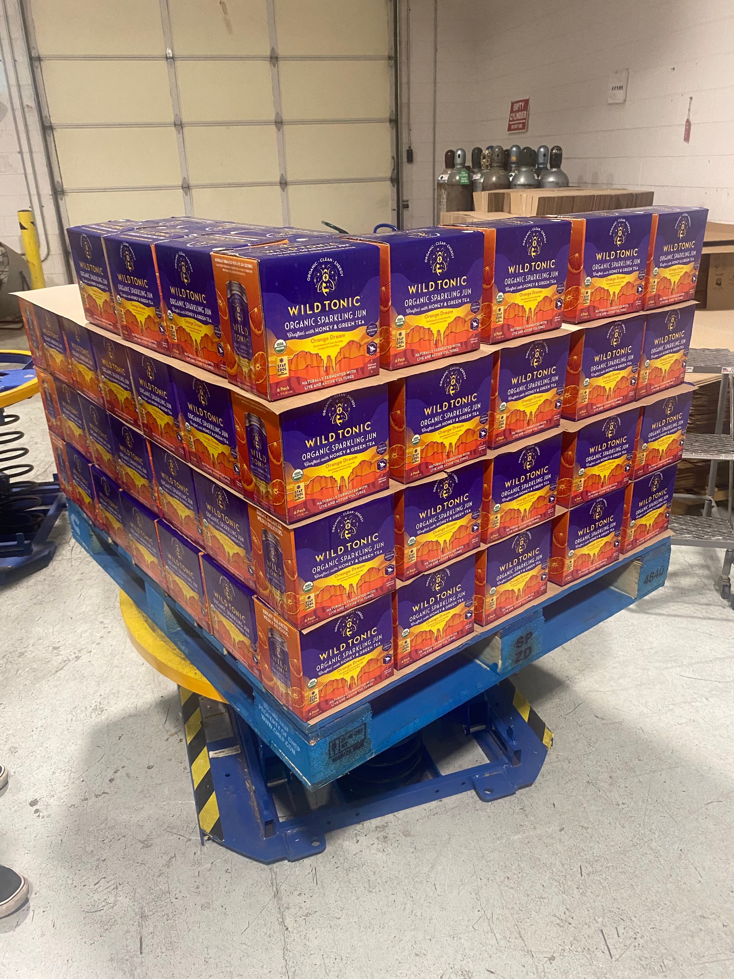 Stack of cereal boxes on a blue hand truck in a store, with a tiled wall in the background.