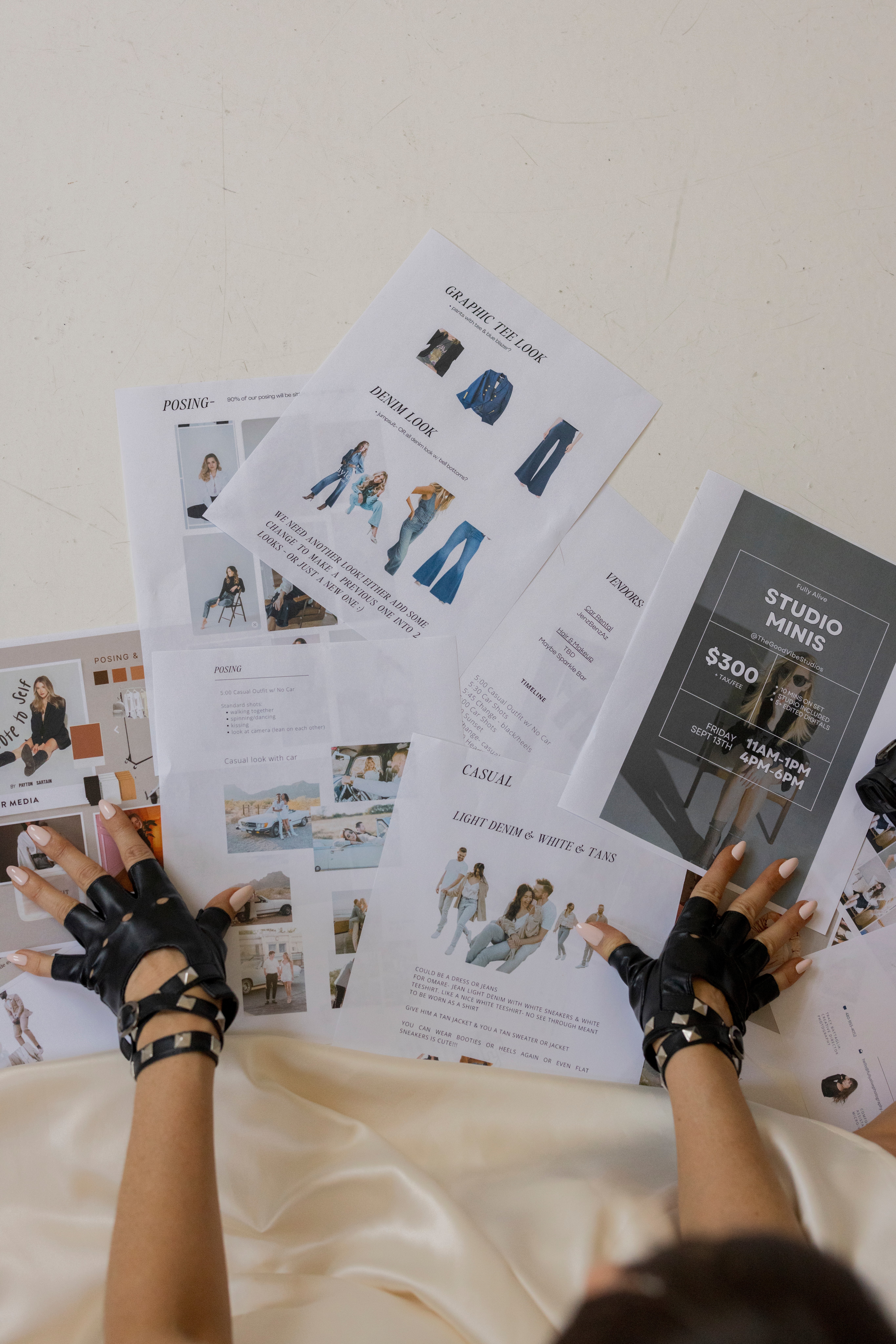Person's hands wearing black gloves, holding and browsing fashion magazines on a white surface.