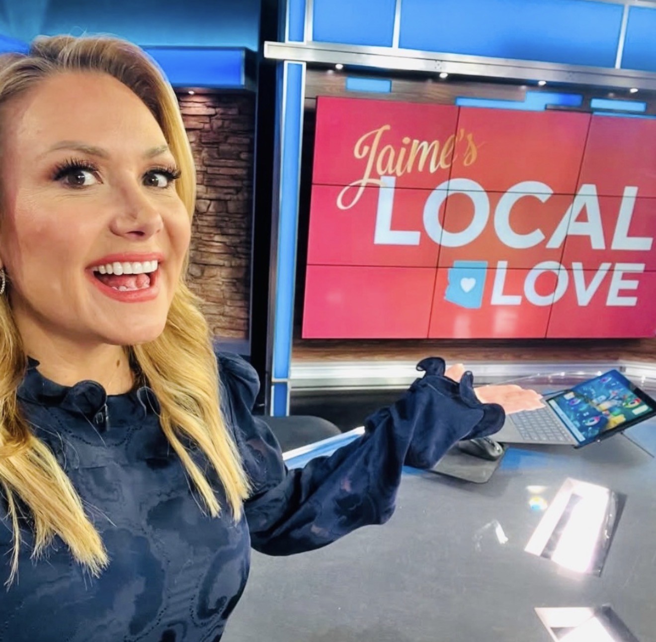 Woman with blonde hair smiling and pointing at a screen displaying 'Jaime's LOCAL LOVE'.