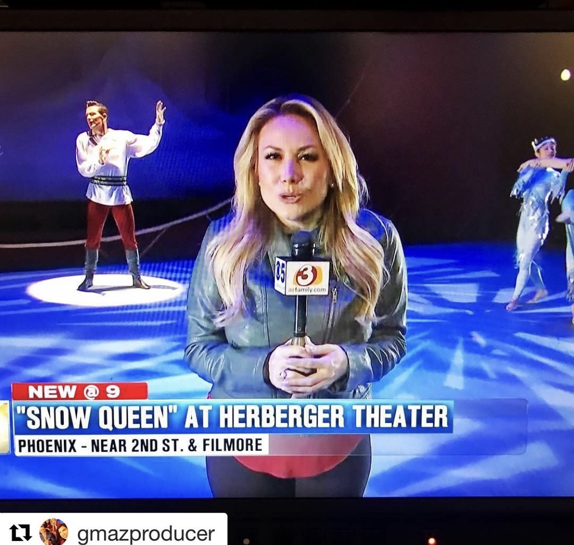 Female reporter holding microphone with two performers in background on ice rink, news banner at bottom, theater sign visible.