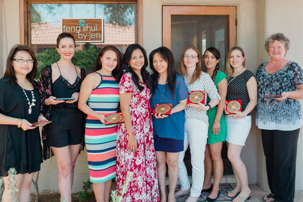 Group of nine women standing outside a building, smiling, holding awards, with a sign in the window behind them.
