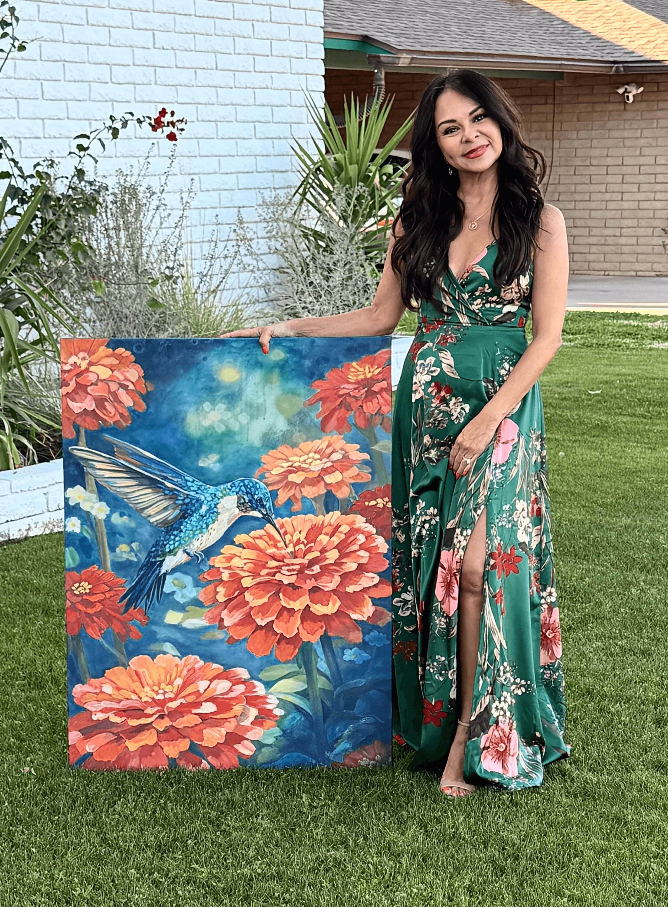 Woman in a green floral dress standing outdoors next to a colorful painting of flowers and a bird, on grass.