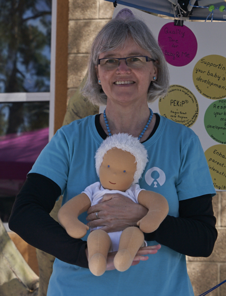 Woman with glasses holding a doll, standing outdoors near a colorful display with circular signs.