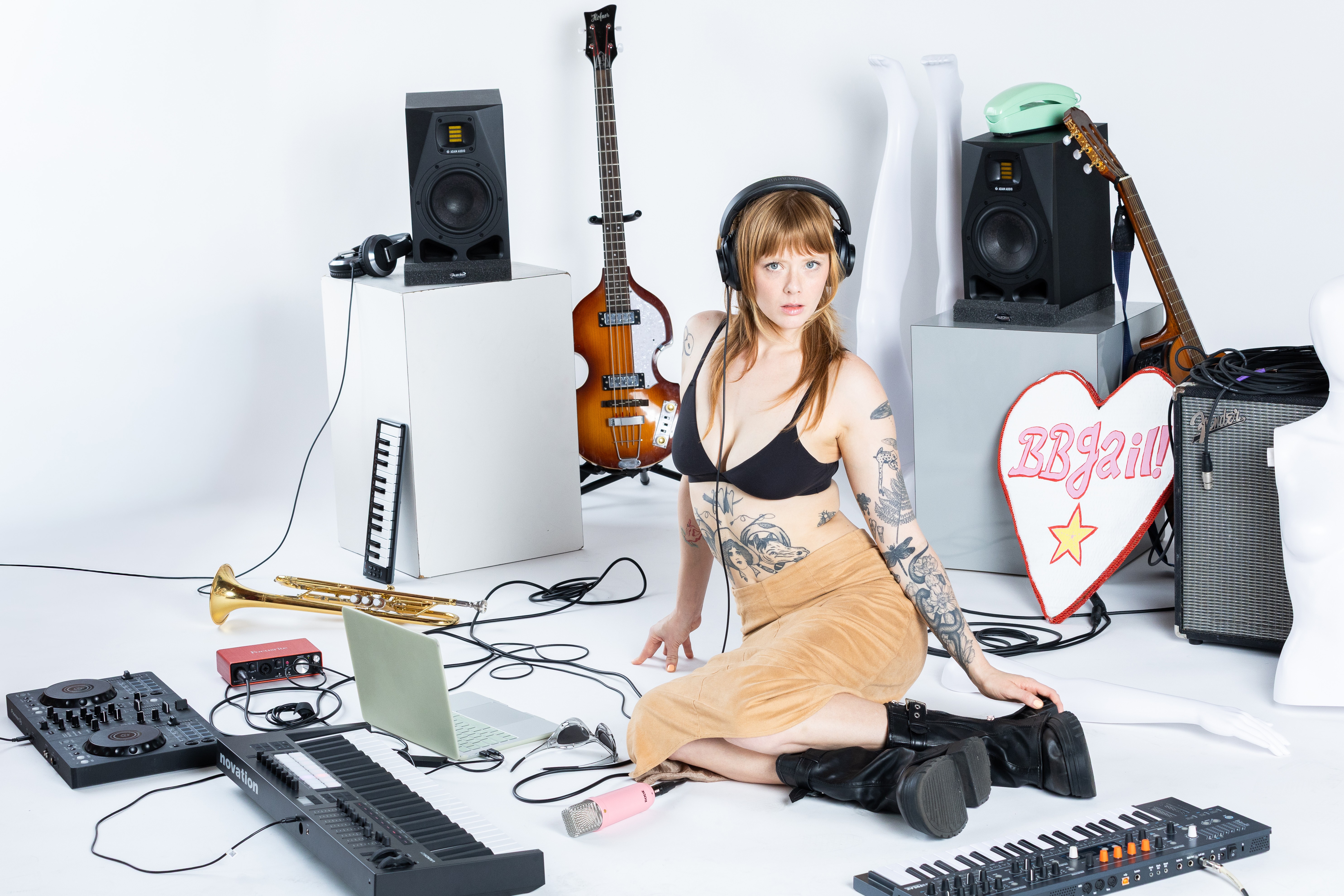 Young woman with tattoos sitting on the floor surrounded by musical equipment and instruments in a studio.