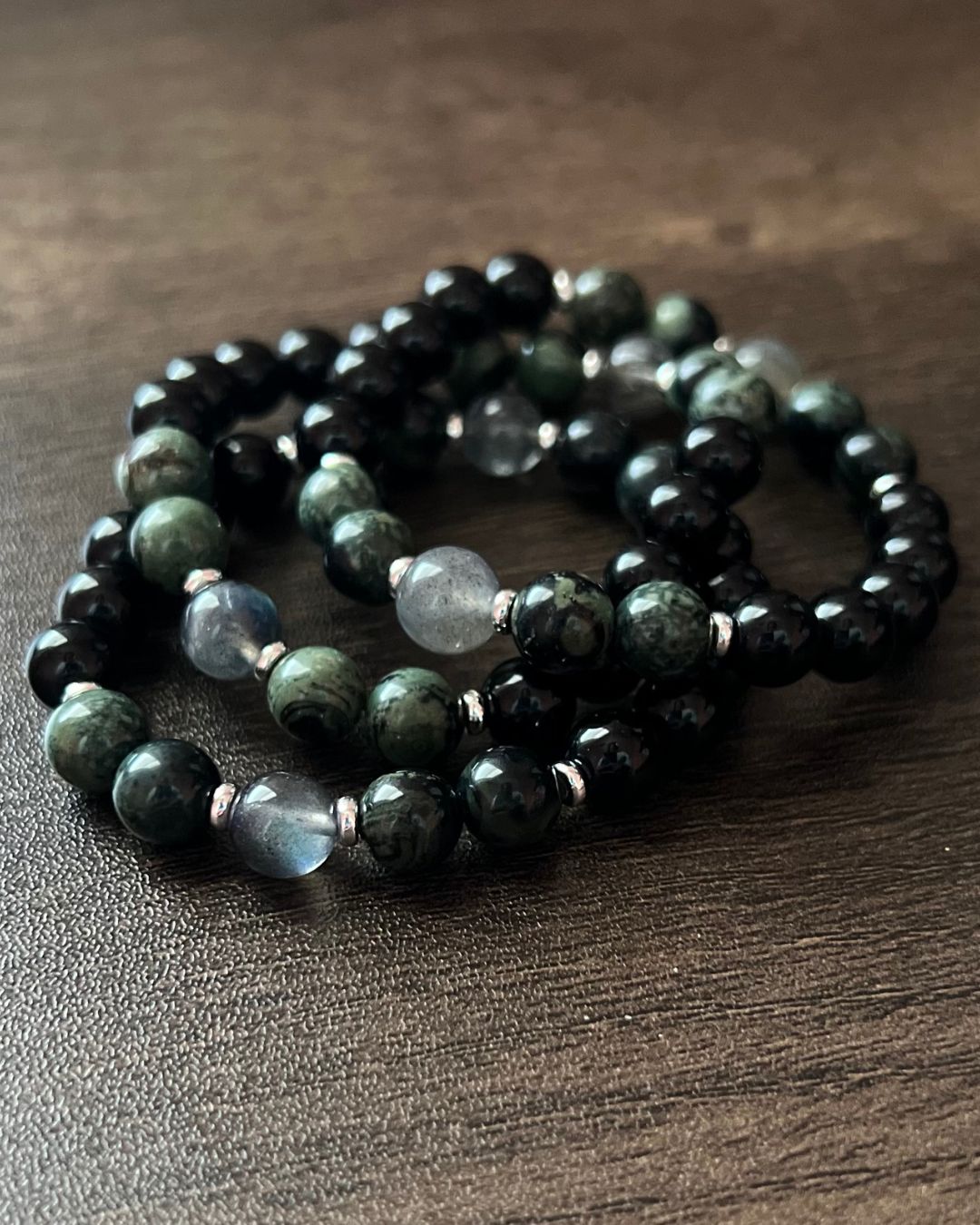 Three beaded bracelets with black and green beads on a wooden surface.