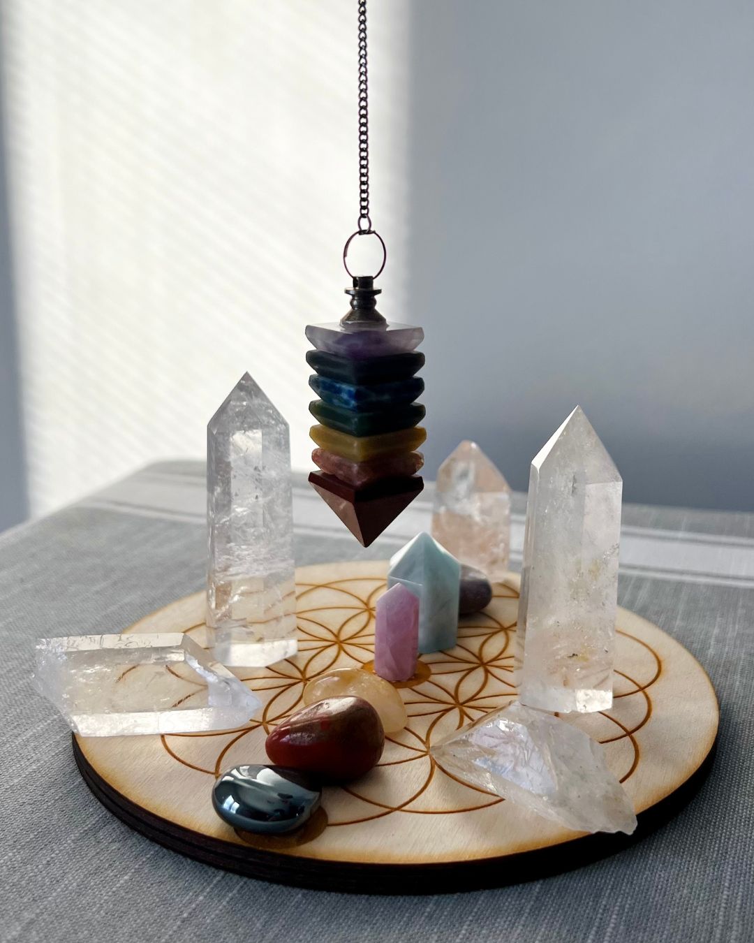 Hanging chakra pendant above a crystal and gemstone display on a round wooden board.