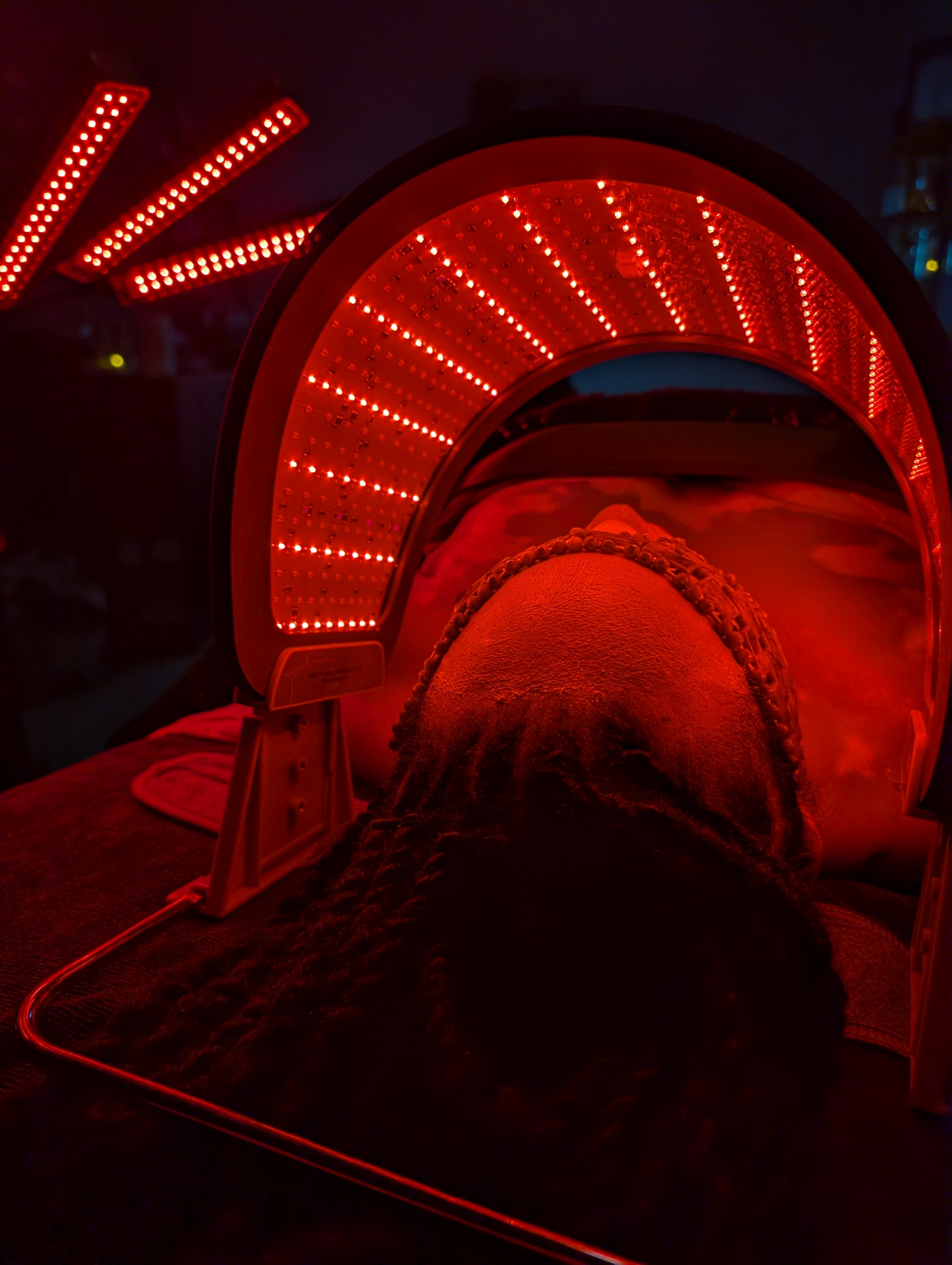 Person's head inside a red light therapy device with illuminated circular and curved lights, in a dark environment.