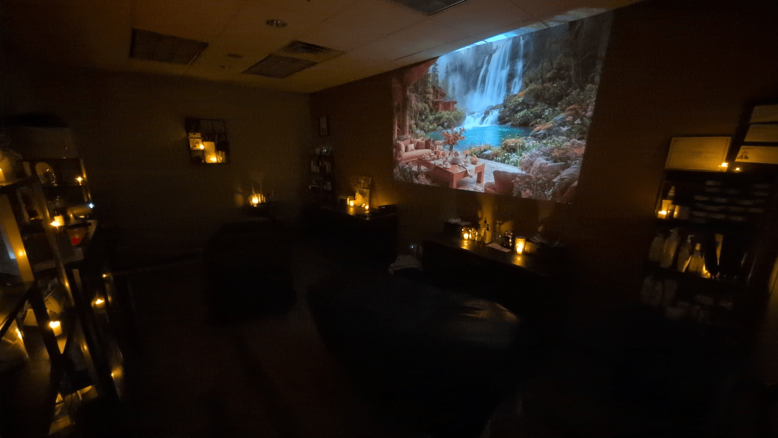 Room with a projected waterfall scene on the wall, dim lighting, candles, and furniture, creating a cozy atmosphere.